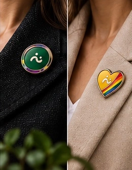 Lifestyle artwork detail: a green Aura Pride pin on a dark jacket and a yellow Heart Pride pin on a cream lapel.